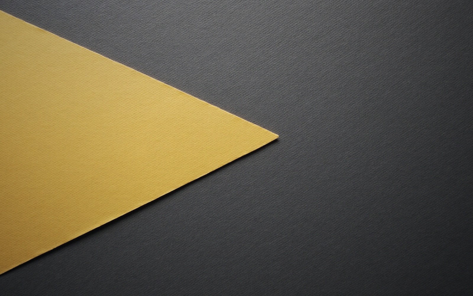 A yellow textured paper corner forms a sharp point against a dark gray background